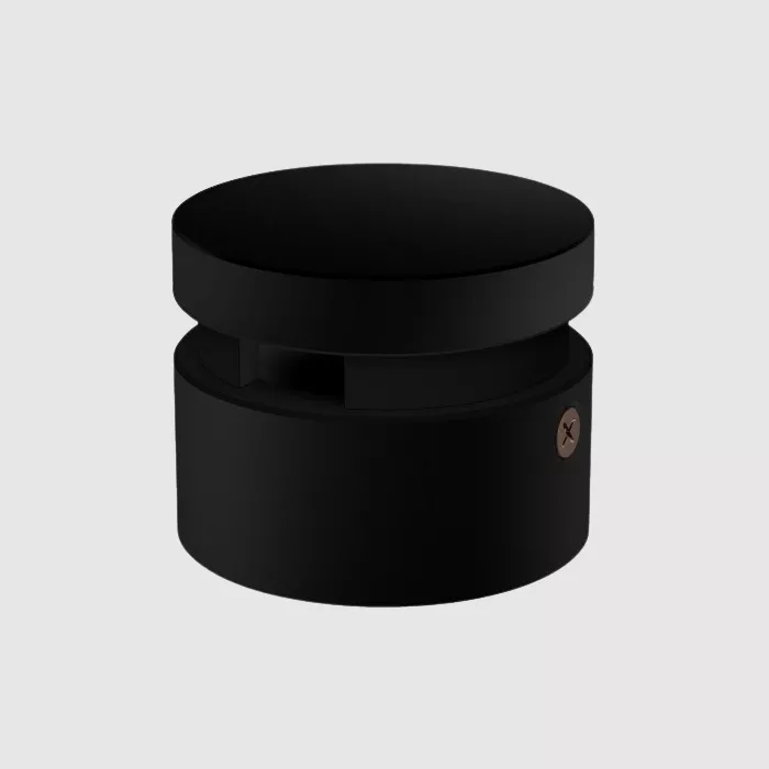 Darc — Un luminaire noir en forme de cylindre avec un couvercle plat et une base légèrement ajourée, marqué d’un petit logo discret sur le côté droit