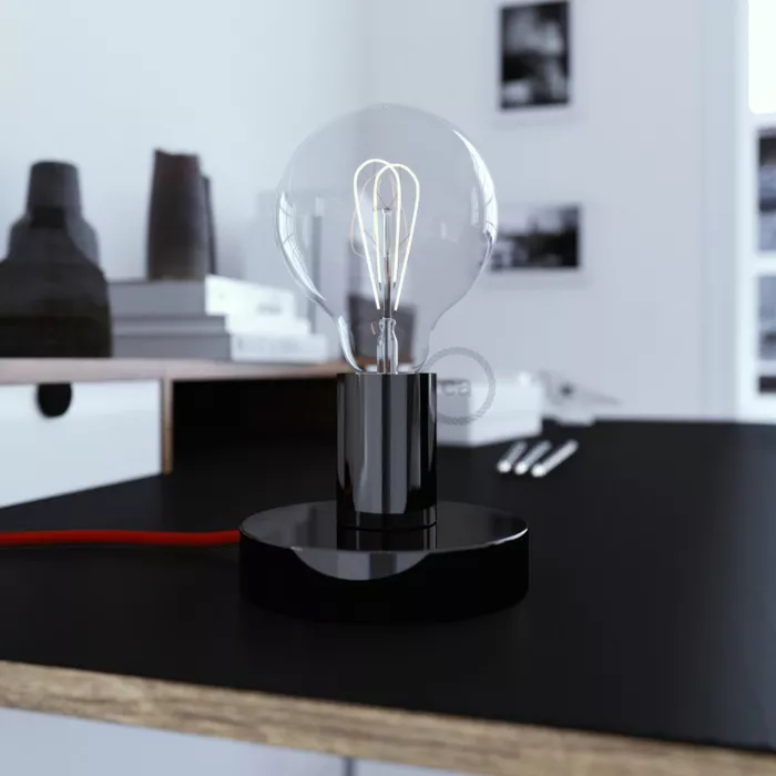 Darc — Une lampe design composée d'une ampoule à filament visible montée sur un pied noir circulaire, posée sur un meuble noir dans un intérieur épuré