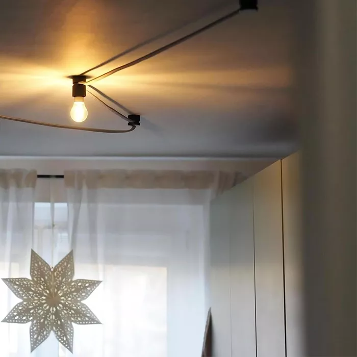 Darc — Une lampe à ampoule claire suspendue au plafond par un bras métallique, éclairant une étoile en métal ajouré posée près d'une fenêtre voilée de