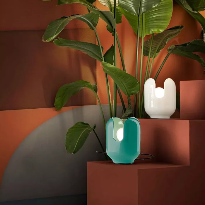 Darc — Une plante verte luxuriante en pot est éclairée par une lampe design turquoise à lumière douce, posée sur une étagère en bois et métal dans un