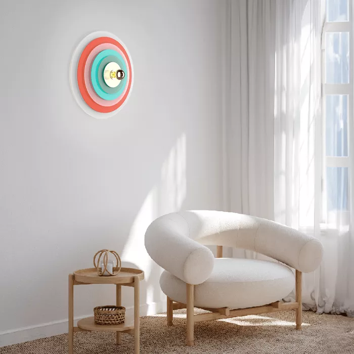 Darc — Applique murale circulaire à trois cercles concentriques colorés en rouge, turquoise et bleu, fixée sur un mur clair près d’un fauteuil blanc e