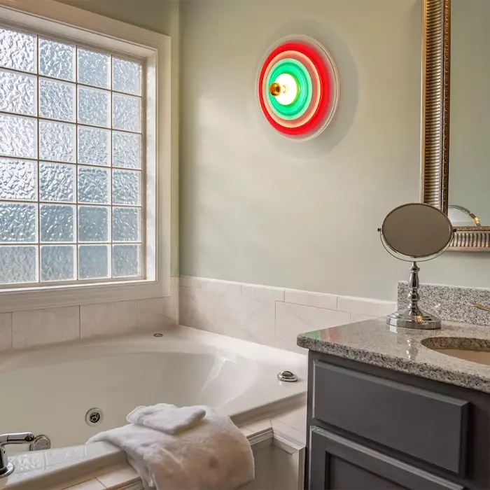 Darc — Une salle de bain élégante dotée d’un éclairage mural circulaire aux couleurs rouge et vert, d’une baignoire blanche remplie d’eau avec une ser
