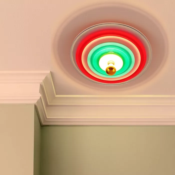 Darc — Un luminaire encastré dans un plafond blanc, entouré d’un cadre circulaire aux dégradés de couleurs rouge et vert, diffusant une lumière douce