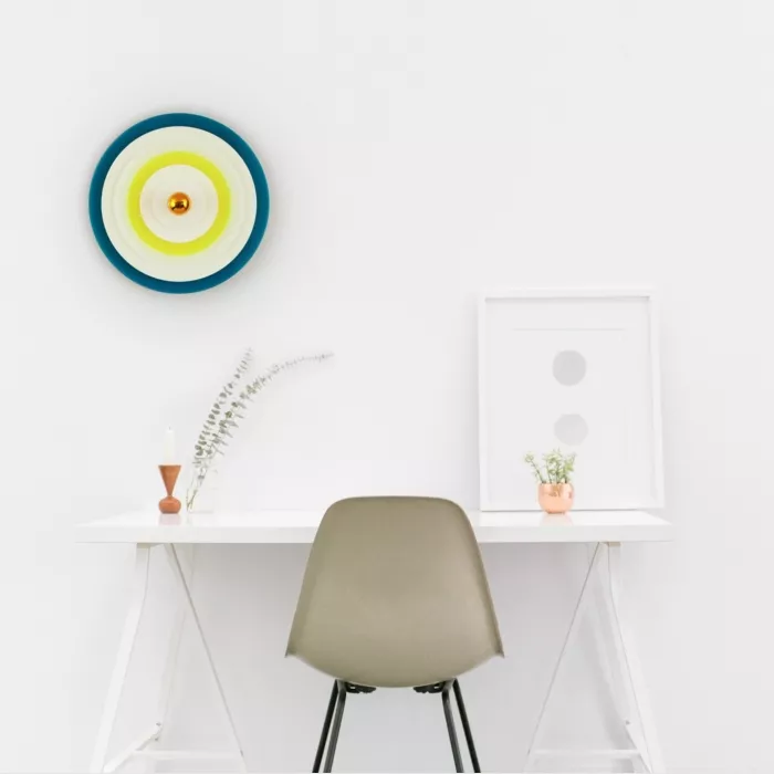 Darc — Un espace de travail épuré composé d'une table transparente en forme de triangle, une chaise beige à structure noire, une cible murale aux coul