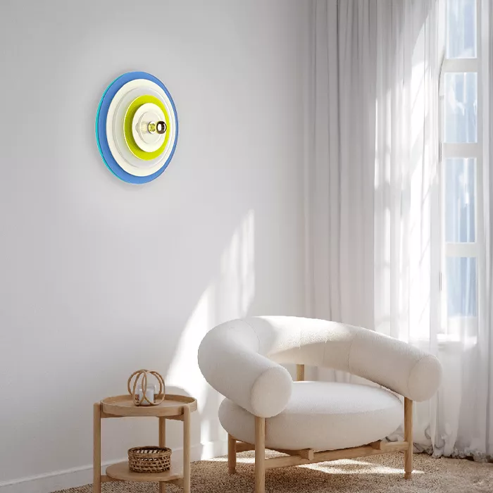 Darc — Une applique murale circulaire aux couleurs vives, composée de trois cercles concentriques bleu turquoise, blanc et jaune, fixée sur un mur bla