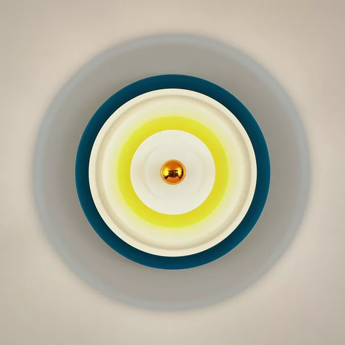 Darc — Applique murale circulaire avec un centre lumineux doré entouré d’un dégradé jaune pâle et d’un anneau bleu foncé, fixée sur un mur clair