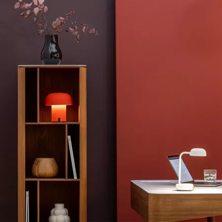 Darc — Une étagère en bois clair avec trois niveaux : en haut, un vase bleu contenant une fleur rose, au centre une lampe rouge et quelques livres, en