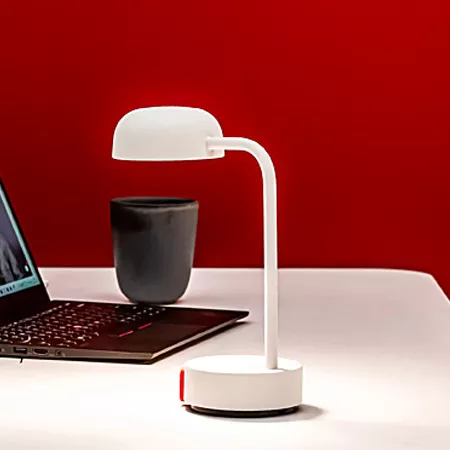 Darc — Une lampe de bureau blanche et élégante, avec une base circulaire et un bras articulé, posée sur un bureau blanc à côté d’un ordinateur portabl