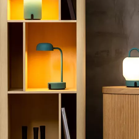 Darc — Une lampe design verte à bras articulé posée sur une étagère en bois clair, éclairant un espace avec une lumière douce et chaude, accompagnée d