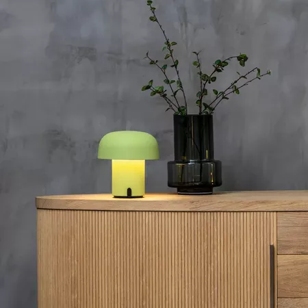 Darc — Une lampe design en forme de champignon vert lumineux posée sur un meuble en bois clair, accompagnée d'un vase noir contenant une plante verte