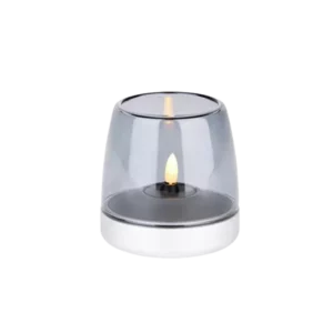Darc — Une bougie allumée protégée par un globe transparent en verre, posée sur un support blanc circulaire, créant une lumière douce et tamisée