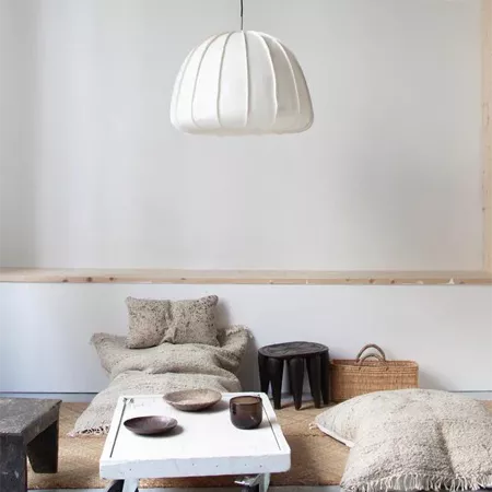 Darc — Un salon épuré avec une lampe suspension blanche en forme de dôme à plusieurs plis suspendue au plafond, une table basse blanche en bois brut,