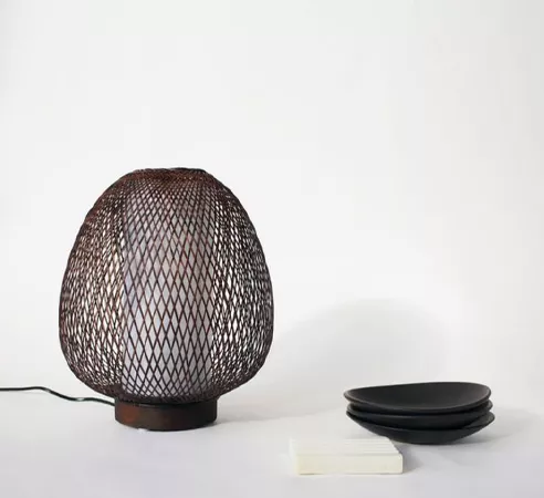 Darc — Lampe design en forme ovale composée d’un treillis métallique fin et d’une base en bois sombre, posée sur une surface blanche avec trois platea