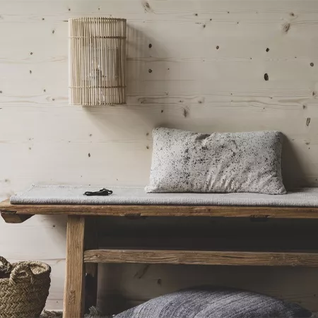Darc — Un lit bas en bois clair posé contre un mur en bois texturé, surmonté d'une suspension murale en bambou tressé. Sur le lit, un coussin gris tex