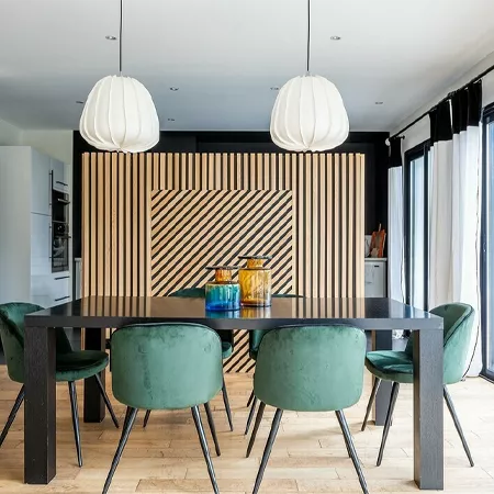 Darc — Une salle à manger élégante équipée d’une table noire rectangulaire entourée de six chaises en velours vert. Deux suspensions lumineuses en for