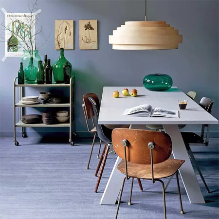 Darc — Une salle à manger épurée où une table blanche centrale est entourée de quatre chaises en cuir vieilli et structure métallique. Un luminaire su