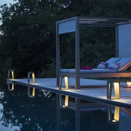 Darc — Une cabane en bois clair surplombant une piscine rectangulaire, entourée de quatre petits luminaires design en forme de piédestaux. À l’intérie
