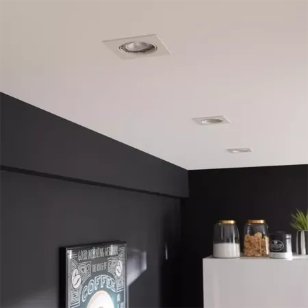 Darc — Deux luminaires encastrés dans un plafond blanc au-dessus d'un plan de travail noir, avec des bocaux et une plante à droite et un cadre photo '
