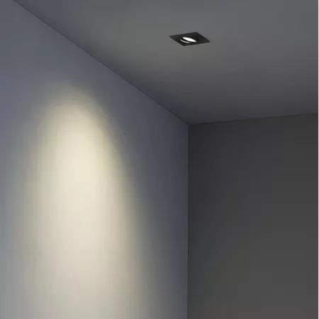 Darc — Un spot encastré noir fixé au plafond projette une lumière douce et ovale sur un mur gris clair, créant une ambiance lumineuse et moderne.