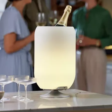 Darc — Un seau à champagne transparent et moderne contenant une bouteille de vin blanc, posée sur une table avec des verres à vin à proximité. Deux pe