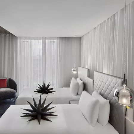 Darc — Une chambre d'hôtel minimaliste et lumineuse avec un lit king size équipé d'une tête de lit en cuir blanc texturé. Des suspensions lumineuses e