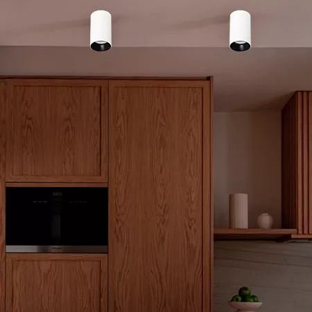 Darc — Une cuisine moderne avec deux spots lumineux encastrés au plafond, un meuble haut en bois clair intégrant un micro-ondes noir, et un petit bol