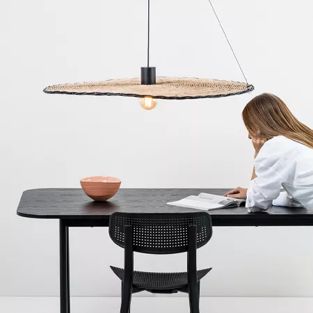 Darc — Une personne est assise à une table noire minimaliste, travaillant sur un document ouvert. Au-dessus de la table, un luminaire suspendu en form