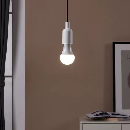 Darc — Une applique suspendue blanche et minimaliste diffuse une lumière douce et chaude dans un coin de pièce aux murs beiges, près d'une étagère ave