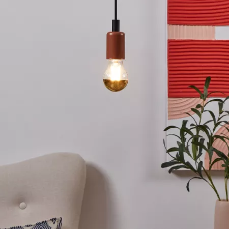Darc — Une applique murale en forme de globe en cuivre suspendue au plafond, éclairée par une ampoule à lumière chaude, posée devant un canapé beige e