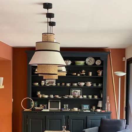 Darc — Armoire noire en bois aux étagères remplies de tasses, théières et assiettes colorées, surmontée d'un luminaire suspendu design à plusieurs aba
