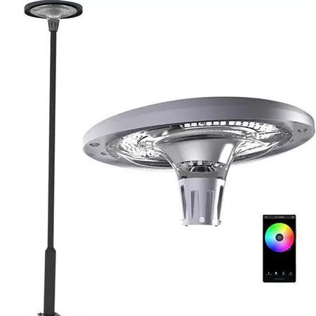 Darc — Un projecteur extérieur moderne en métal noir fixé sur un mât, avec un large diffuseur circulaire et une base lumineuse. À droite, une télécomm