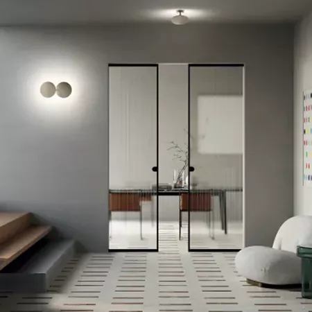 Darc — Une pièce lumineuse aux murs gris clair, équipée d’une porte coulissante vitrée reflétant un petit espace avec table basse et plante, éclairée