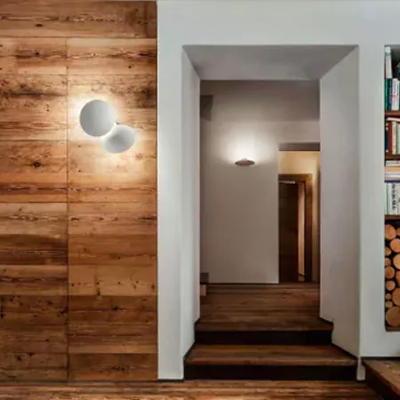 Darc — Un couloir lumineux avec un mur en bois brut texturé à gauche, deux appliques murales rondes blanches éclairant l’espace, et une porte blanche