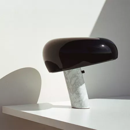 Darc — Une lampe design noire en forme d'œuf, posée sur un pied en marbre blanc texturé, éclairant un espace épuré avec une lumière douce