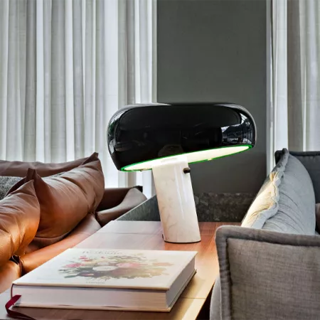 Darc — Une lampe design moderne en forme de capsule noire posée sur un pied blanc, émettant une douce lumière verte, placée sur une table basse entre