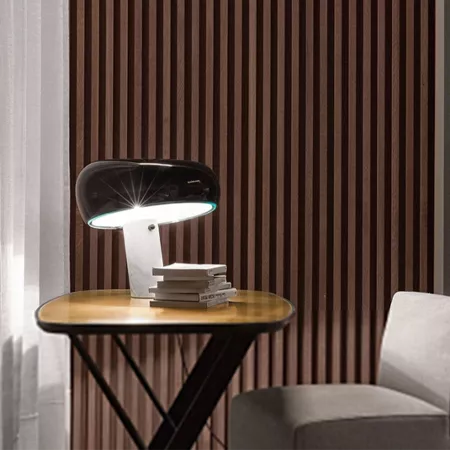 Darc — Une lampe design à pied noir et blanc, posée sur une table en bois clair, éclairant un espace de travail minimaliste avec des livres empilés à