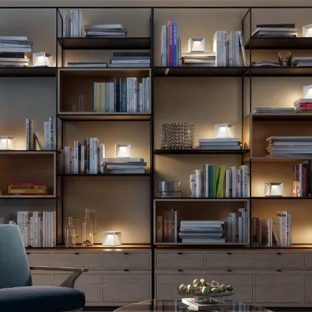 Darc — Une bibliothèque murale en métal noir et bois clair, éclairée par des spots intégrés, remplie de livres, magazines et quelques objets décoratif