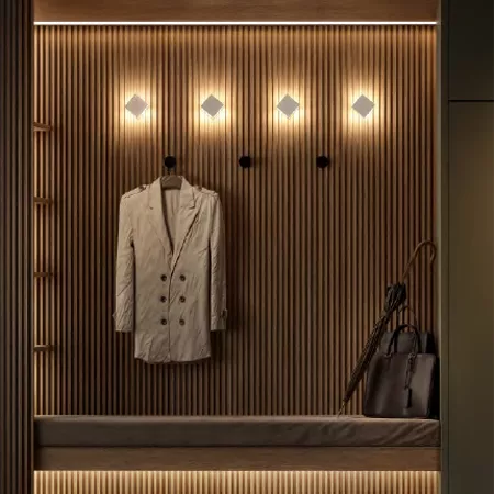 Darc — Un blazer beige à boutons noirs est suspendu à une patère dans un dressing mural en bois clair, éclairé par des spots lumineux disposés en rang