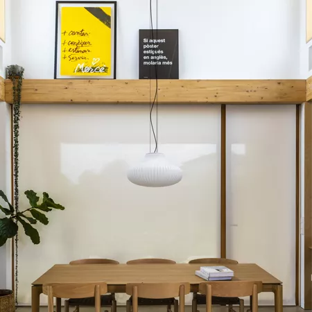 Darc — Une pièce lumineuse avec une longue table en bois clair entourée de quatre chaises, une suspension lumineuse blanche en forme de nuage au plafo