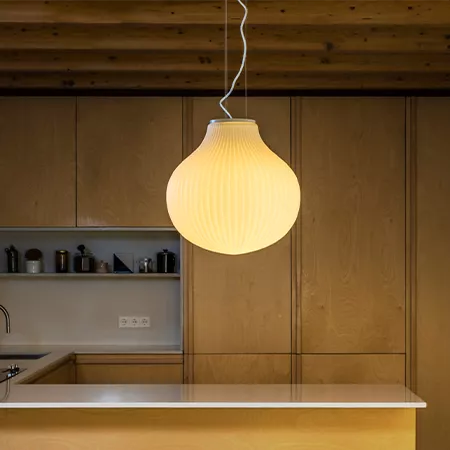 Darc — Une lampe suspendue en forme de globe en verre strié, suspendue par un fil métallique au-dessus d'un plan de travail de cuisine en bois clair,