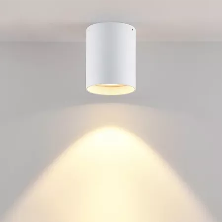 Darc — Un projecteur encastré blanc au plafond diffuse une lumière chaude et douce en forme de cercle sur un mur clair.
