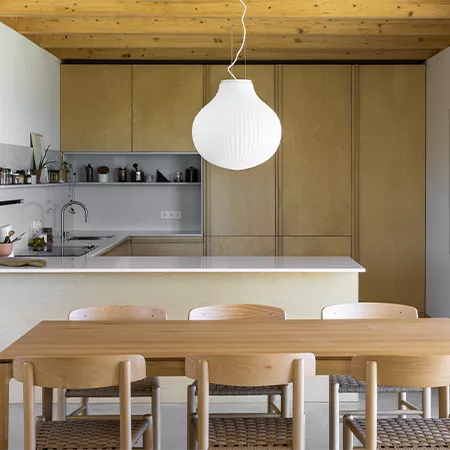 Darc — Une cuisine lumineuse aux meubles en bois clair, avec un îlot central en blanc, des tabourets en bois et un luminaire suspendu en forme de glob