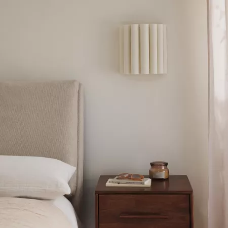 Darc — Une chambre épurée avec un lit à tête de lit beige, une table de chevet en bois sombre sur laquelle reposent un livre ouvert, une paire de lune