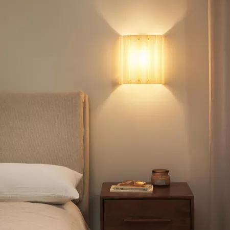 Darc — Une chambre épurée avec un lit bien fait, une tête de lit en tissu beige, une table de chevet en bois sombre et un éclairage mural doux encadré