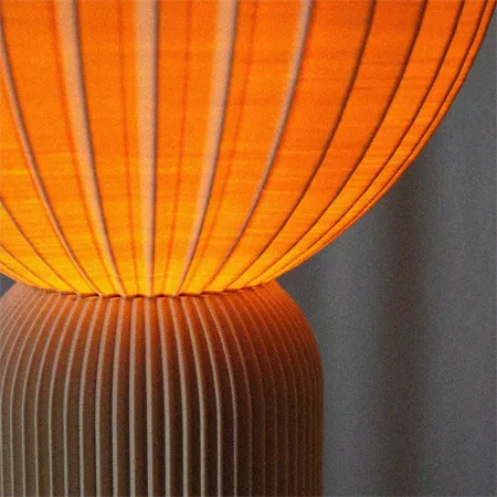 Darc — Une lampe design avec un abat-jour en forme de plis lumineux, éclairant une lumière orange chaude et enveloppante, montée sur une base en métal