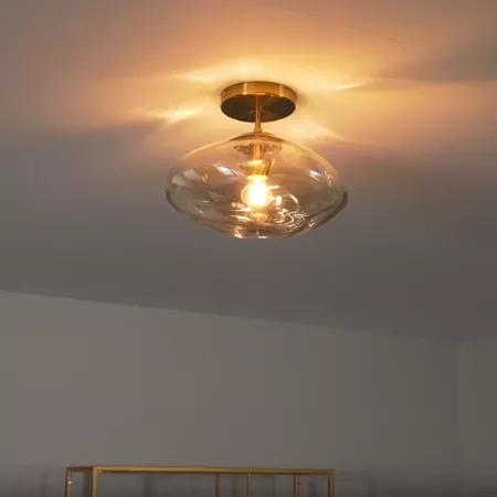 Darc — Applique murale en forme d’ovale translucide suspendue au plafond, éclairée par une ampoule à lumière chaude, dans une pièce aux murs clairs.