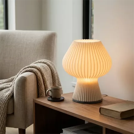 Darc — Lampe en céramique texturée de forme organique posée sur une table basse en bois, éclairant une tasse à café et un livre, avec un fauteuil gris