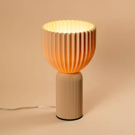 Darc — Lampe design en forme de vase avec une structure ondulée verticale et horizontale, émettant une lumière chaude et douce sur un fond neutre.